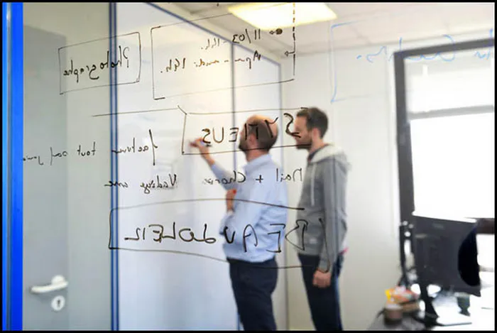 Vue artistique de deux collaborateurs écrivant sur un tableau, scène observée à travers une vitre