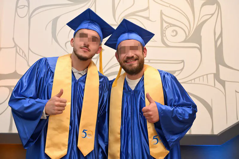 Portrait de deux diplômés ISTELI Lyon en toge bleue faisant le pouce levé
