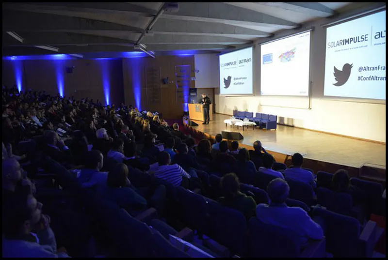 Amphithéâtre rempli lors d’une conférence professionnelle sur le projet Solar Impulse, avec orateur sur scène face au public