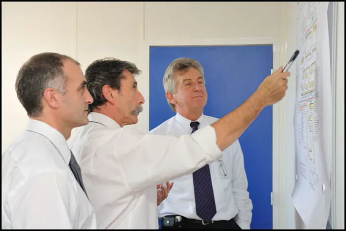 Trois collaborateurs en réunion de travail devant un tableau, scène de collaboration en entreprise