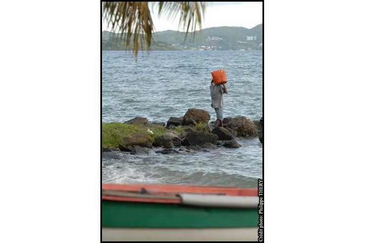 Bateau de pêcheur et pêcheur portant un baril sur la jetée, Martinique